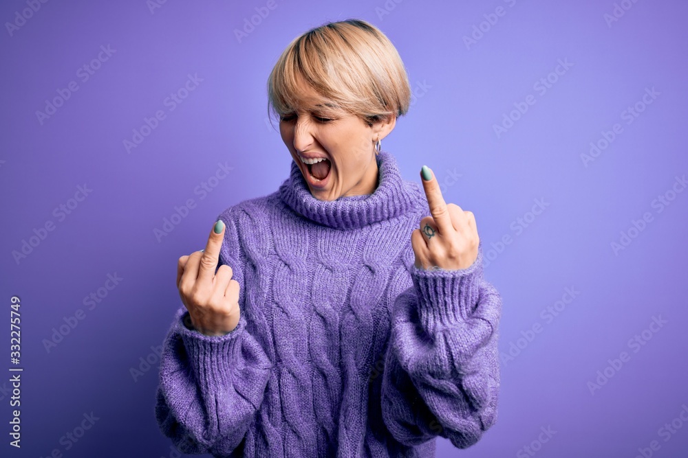 Young blonde woman with short hair wearing winter turtleneck sweater over purple background Showing middle finger doing fuck you bad expression, provocation and rude attitude. Screaming excited Young blonde woman with short hair wearing winter turtleneck sweater over purple background Showing middle finger doing fuck you bad expression, provocation and rude attitude. Screaming excited