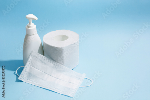 Antiseptic sanitizer gel, medicine face mask and toilet paper roll on blue background