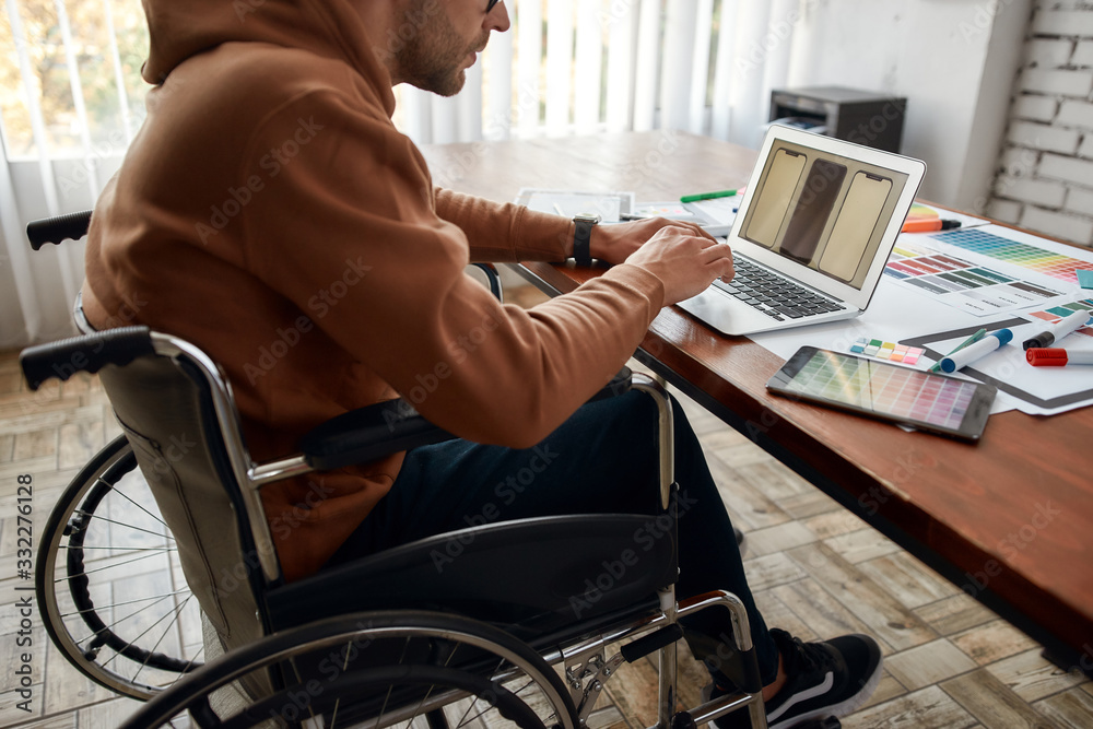 Side view of young male UX UI designer in a wheelchair developing new ...