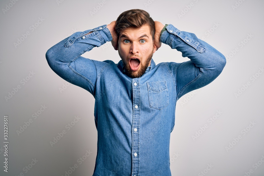 Young handsome blond man with beard and blue eyes wearing casual denim shirt Crazy and scared with hands on head, afraid and surprised of shock with open mouth Young handsome blond man with beard and blue eyes wearing casual denim shirt Crazy and scared with hands on head, afraid and surprised of shock with open mouth