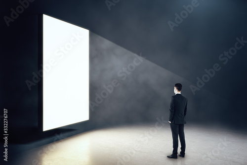 Businessman looking on blank glowing poster in interior