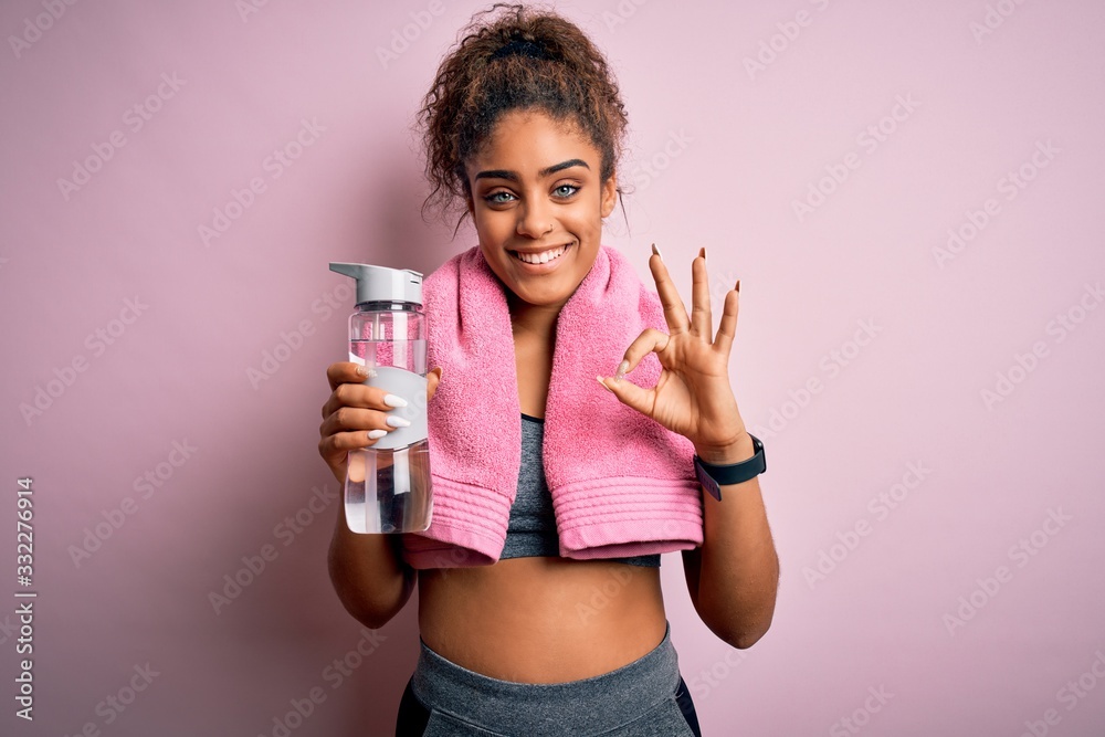 Young african american sporty girl doing sport wearing towel drinking bottle of water doing ok sign with fingers, excellent symbol Young african american sporty girl doing sport wearing towel drinking bottle of water doing ok sign with fingers, excellent symbol
