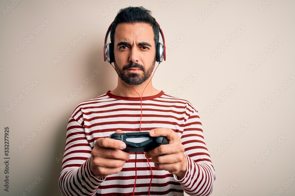 Young handsome gamer man with beard playing video game using joystick and headphones with a confident expression on smart face thinking serious Young handsome gamer man with beard playing video game using joystick and headphones with a confident expression on smart face thinking serious