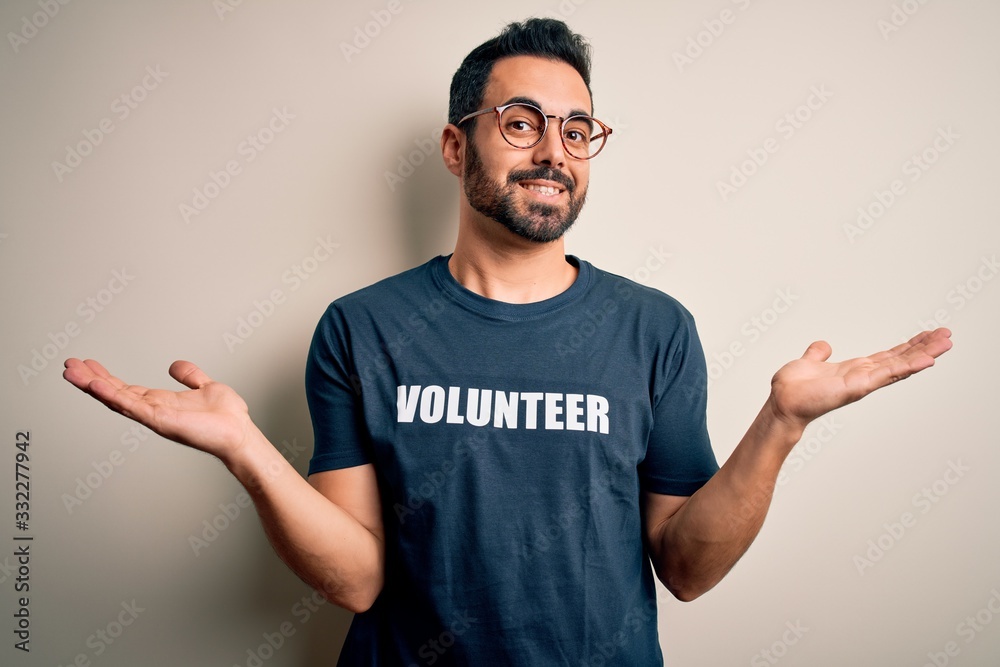 Handsome man with beard wearing t-shirt with volunteer message over white background smiling showing both hands open palms, presenting and advertising comparison and balance Handsome man with beard wearing t-shirt with volunteer message over white background smiling showing both hands open palms, presenting and advertising comparison and balance