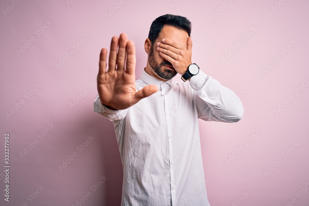 Young handsome man with beard wearing casual shirt standing over pink background covering eyes with hands and doing stop gesture with sad and fear expression. Embarrassed and negative concept. Young handsome man with beard wearing casual shirt standing over pink background covering eyes with hands and doing stop gesture with sad and fear expression. Embarrassed and negative concept.