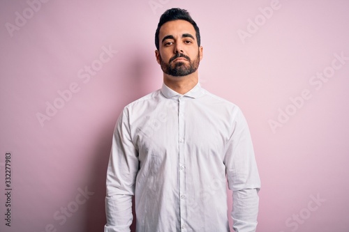 Young handsome man with beard wearing casual shirt standing over pink background depressed and worry for distress, crying angry and afraid. Sad expression.