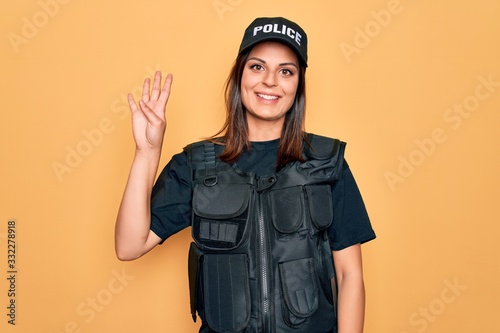 Photo Young beautiful brunette policewoman wearing police uniform bulletproof and cap showing and pointing up with fingers number four while smiling confident and happy