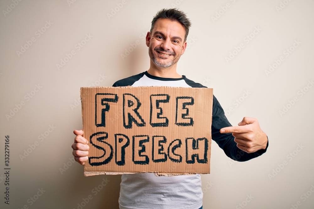Young handsome man asking for rights holding banner with free speech message very happy pointing with hand and finger Young handsome man asking for rights holding banner with free speech message very happy pointing with hand and finger