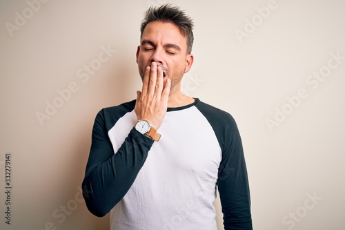 Young handsome man wearing casual t-shirt standing over isolated white background bored yawning tired covering mouth with hand. Restless and sleepiness.