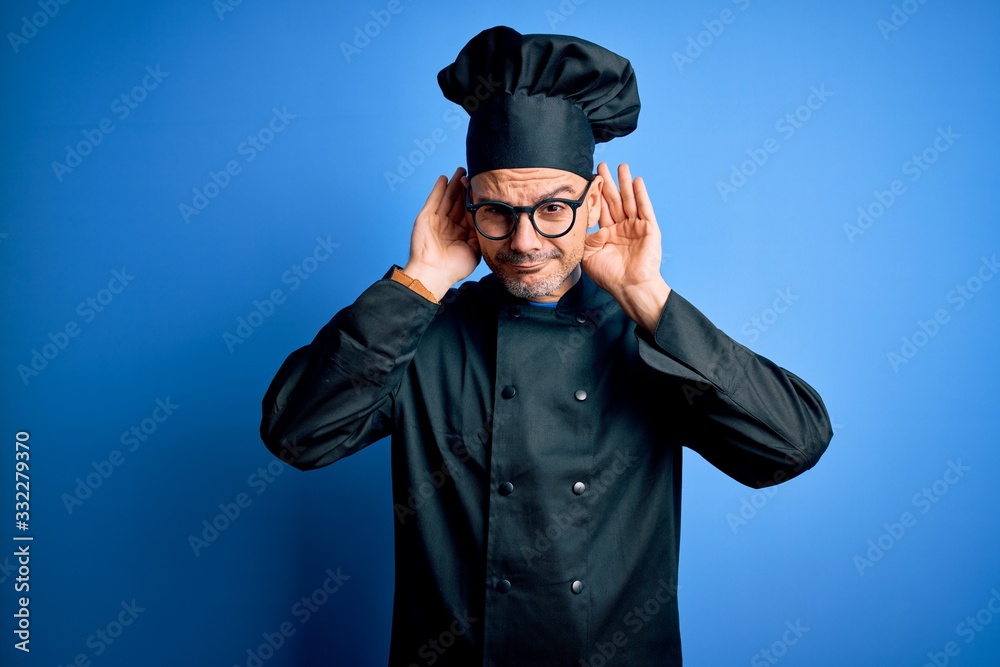 Young handsome chef man wearing cooker uniform and hat over isolated blue background Trying to hear both hands on ear gesture, curious for gossip. Hearing problem, deaf Young handsome chef man wearing cooker uniform and hat over isolated blue background Trying to hear both hands on ear gesture, curious for gossip. Hearing problem, deaf