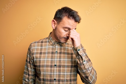 Young handsome man wearing casual shirt standing over isolated yellow background tired rubbing nose and eyes feeling fatigue and headache. Stress and frustration concept. © Krakenimages.com