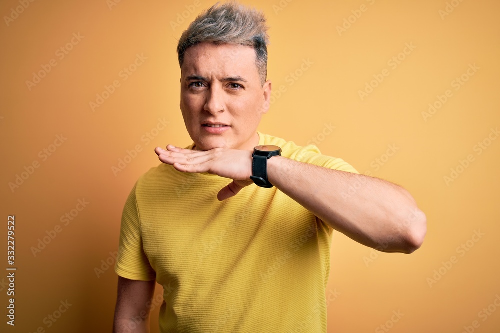 Young handsome modern man wearing yellow shirt over yellow isolated background cutting throat with hand as knife, threaten aggression with furious violence Young handsome modern man wearing yellow shirt over yellow isolated background cutting throat with hand as knife, threaten aggression with furious violence