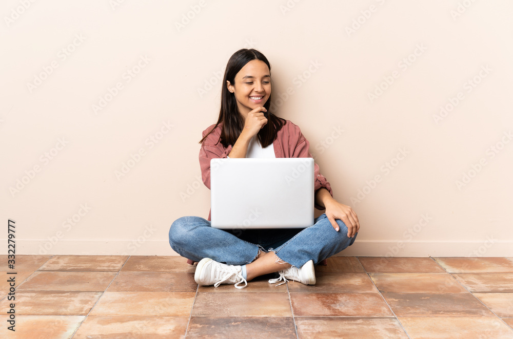 Young mixed race woman with a laptop sitting on the floor looking to the side and smiling Young mixed race woman with a laptop sitting on the floor looking to the side and smiling