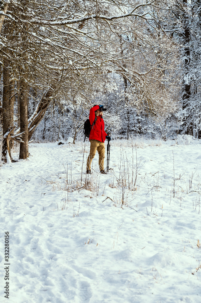 Male photographer in red jacket taking pictures of winter landscape in snowy forest.