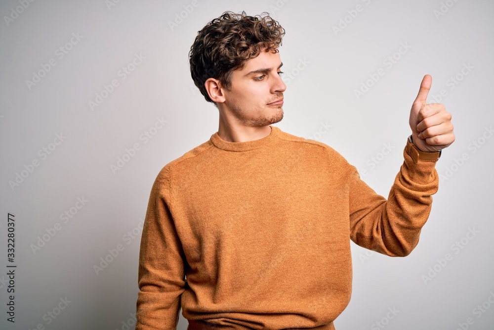 Young blond handsome man with curly hair wearing casual sweater over white background Looking proud, smiling doing thumbs up gesture to the side Young blond handsome man with curly hair wearing casual sweater over white background Looking proud, smiling doing thumbs up gesture to the side