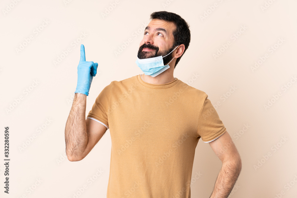 Caucasian man with beard protecting from the coronavirus with a mask and gloves over isolated background pointing up a great idea Caucasian man with beard protecting from the coronavirus with a mask and gloves over isolated background pointing up a great idea