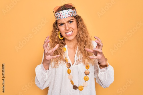 Young beautiful blonde hippie woman with blue eyes wearing sunglasses and accessories Shouting frustrated with rage, hands trying to strangle, yelling mad © Krakenimages.com