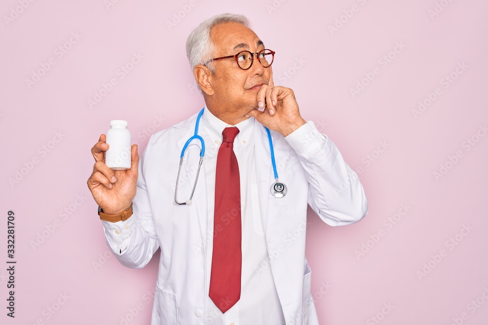 Middle age senior grey-haired doctor man holding prescription pills over pink background serious face thinking about question, very confused idea Middle age senior grey-haired doctor man holding prescription pills over pink background serious face thinking about question, very confused idea