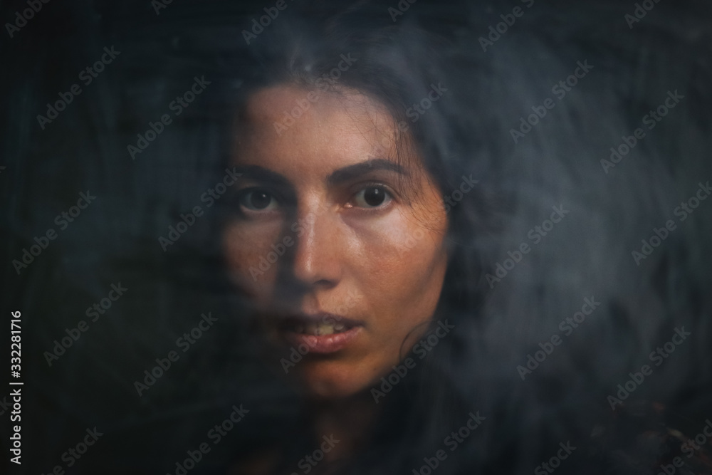 Portrait of feminine young woman with dark hair  with a mysterious look,  posing at camera  in low lights on black background. Antique effect and vintage style.