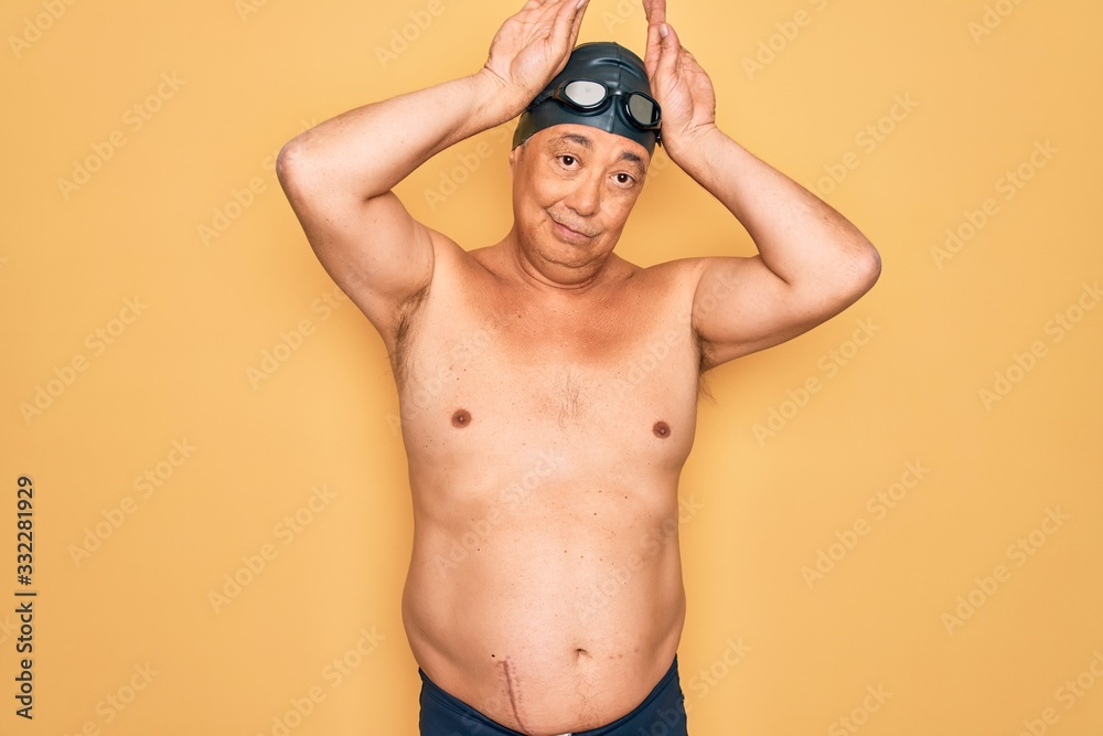 Middle age senior grey-haired swimmer man wearing swimsuit, cap and goggles Doing bunny ears gesture with hands palms looking cynical and skeptical. Easter rabbit concept.