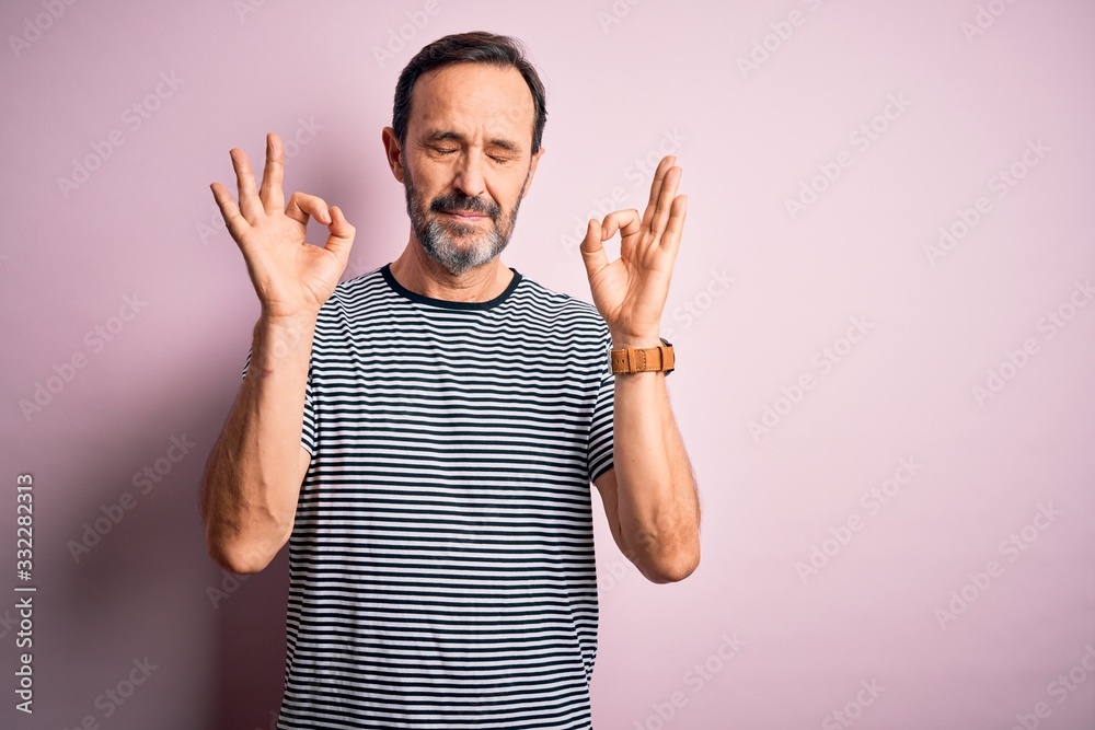 Middle age hoary man wearing casual striped t-shirt standing over isolated pink background relax and smiling with eyes closed doing meditation gesture with fingers. Yoga concept. Middle age hoary man wearing casual striped t-shirt standing over isolated pink background relax and smiling with eyes closed doing meditation gesture with fingers. Yoga concept.