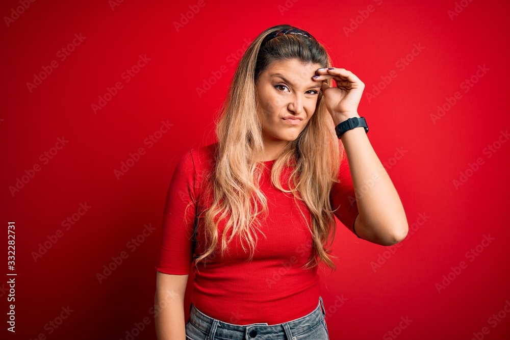 Young beautiful blonde woman wearing casual t-shirt standing over isolated red background worried and stressed about a problem with hand on forehead, nervous and anxious for crisis Young beautiful blonde woman wearing casual t-shirt standing over isolated red background worried and stressed about a problem with hand on forehead, nervous and anxious for crisis