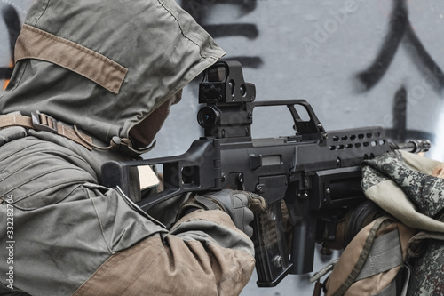 A hired soldier in the hood is aiming from a modern rifle.