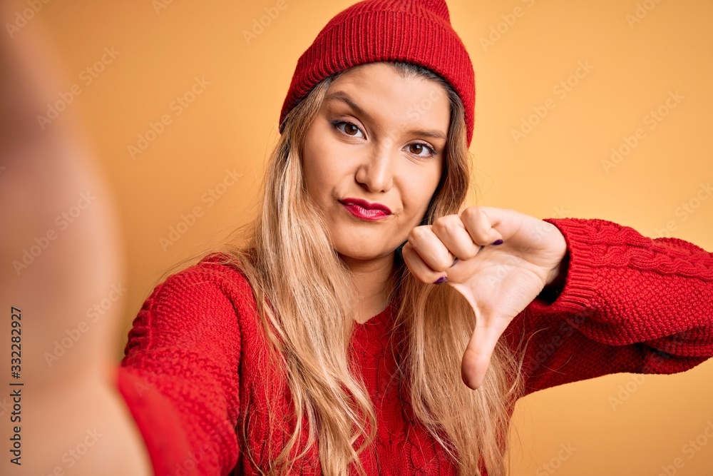 Young beautiful blonde woman making selfie by camera over isolated yellow background with angry face, negative sign showing dislike with thumbs down, rejection concept Young beautiful blonde woman making selfie by camera over isolated yellow background with angry face, negative sign showing dislike with thumbs down, rejection concept