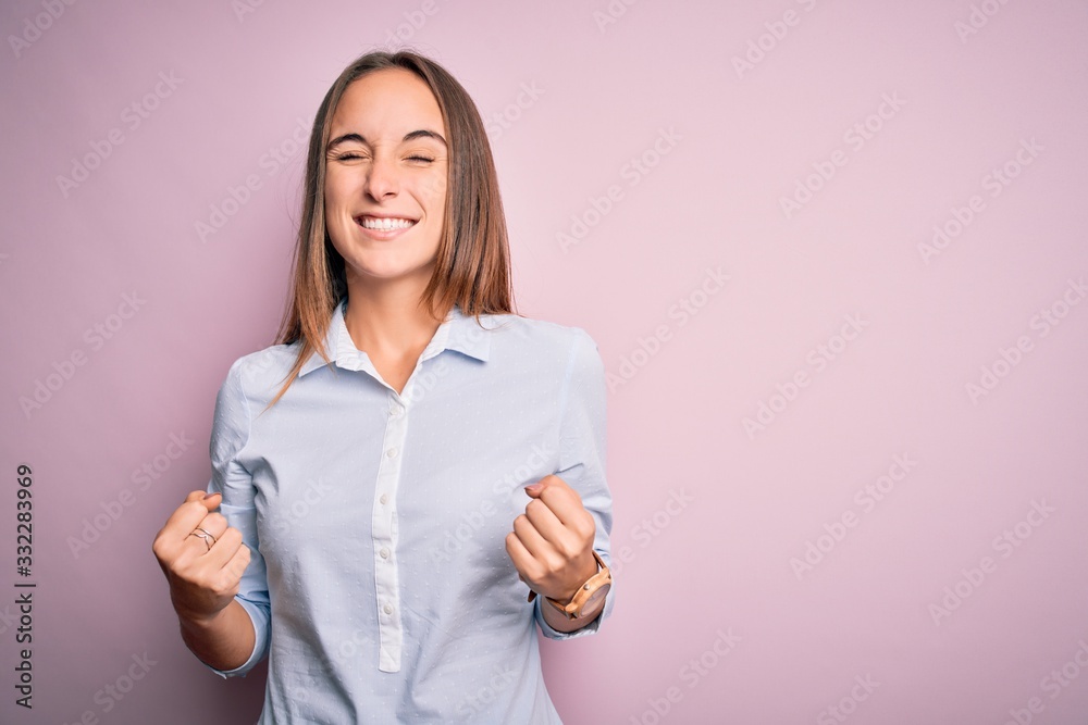 Young beautiful businesswoman wearing elegant shirt standing over isolated pink background very happy and excited doing winner gesture with arms raised, smiling and screaming for success. Celebration Young beautiful businesswoman wearing elegant shirt standing over isolated pink background very happy and excited doing winner gesture with arms raised, smiling and screaming for success. Celebration