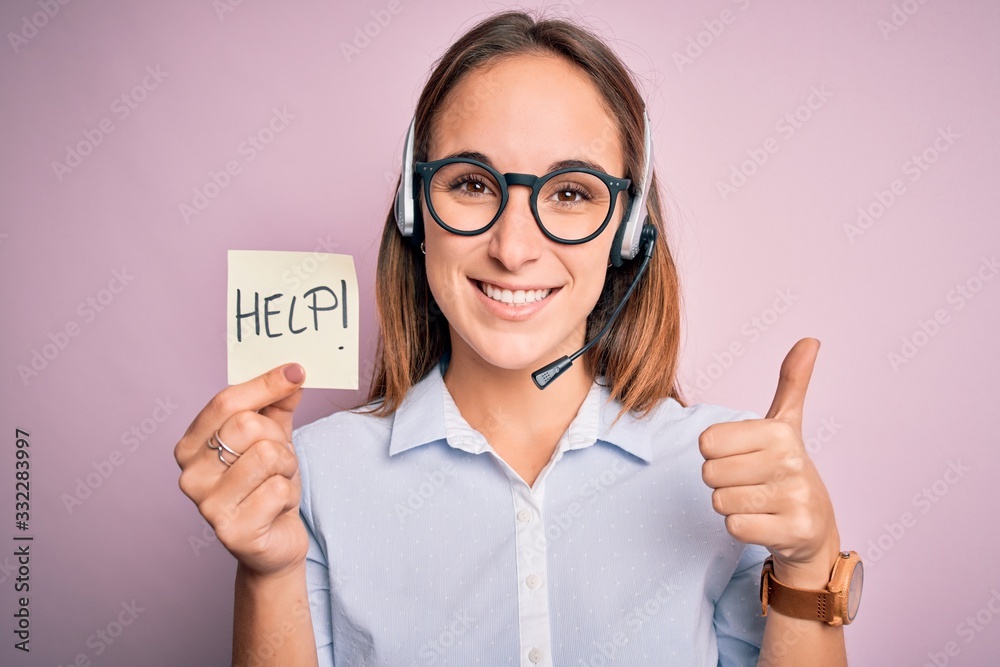 Beautiful call center agent woman working using headset holding help reminder message happy with big smile doing ok sign, thumb up with fingers, excellent sign Beautiful call center agent woman working using headset holding help reminder message happy with big smile doing ok sign, thumb up with fingers, excellent sign
