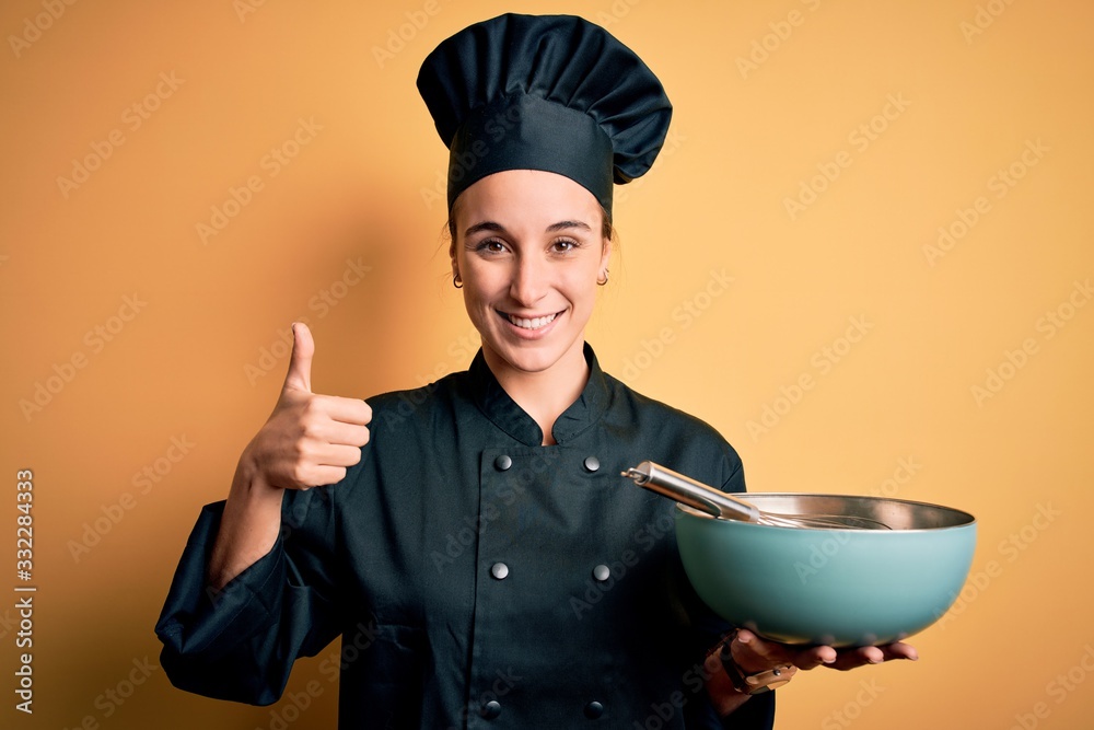 Young beautiful chef woman wearing cooker uniform and hat holding bowl and whisk happy with big smile doing ok sign, thumb up with fingers, excellent sign Young beautiful chef woman wearing cooker uniform and hat holding bowl and whisk happy with big smile doing ok sign, thumb up with fingers, excellent sign