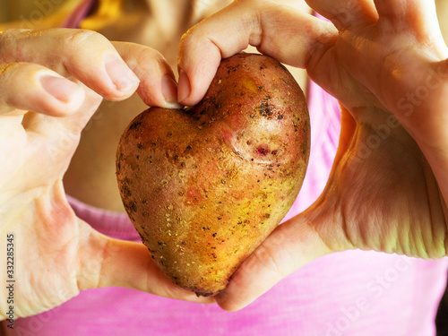 A close-up photo of female fingers holding a heart-shaped potato photo