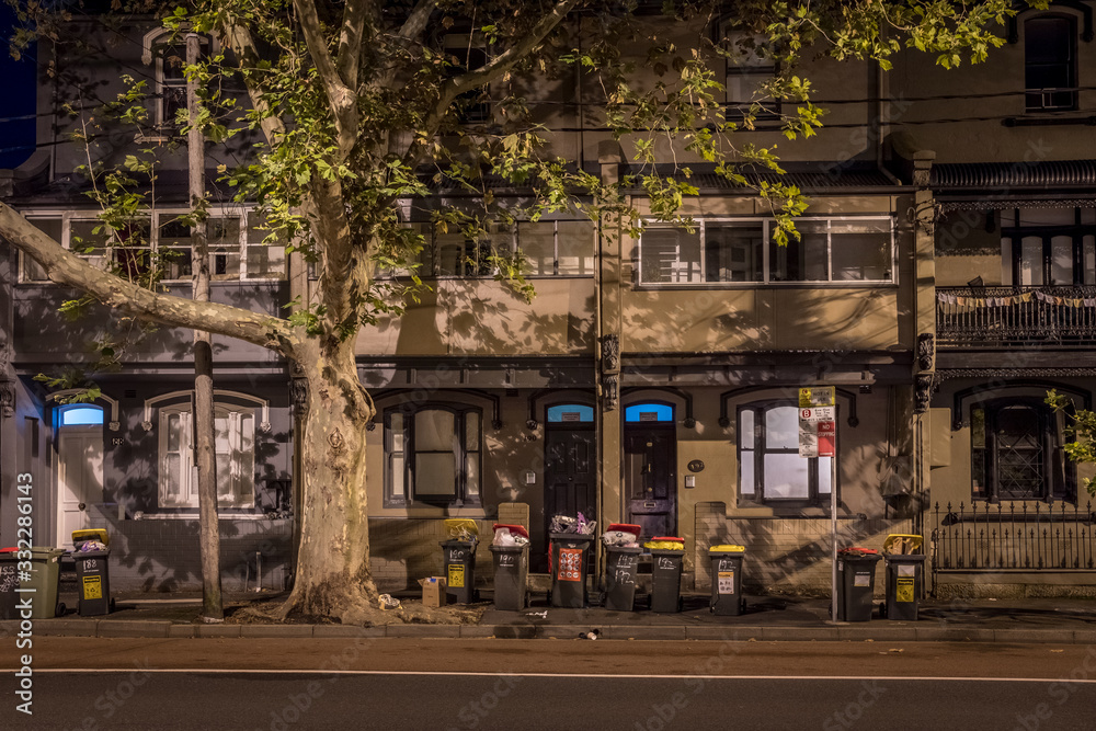 trash cans waiting collection on an old street at night