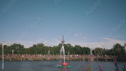 Tomorrowland Belgium connective time lapse of festival guests crossing a bridge accompanied by trees and flower fountains in blue cloudy sky. photo