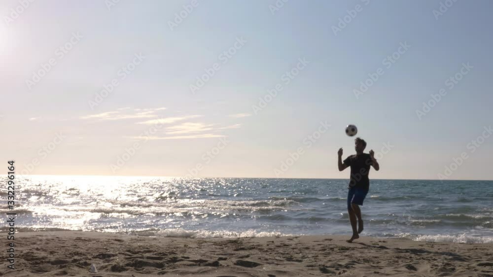 Young man in swimming trunks does tricks dribbling bouncing football on the sea shore at the beach at sunset silhouette Young man in swimming trunks does tricks dribbling bouncing football on the sea shore at the beach at sunset silhouette