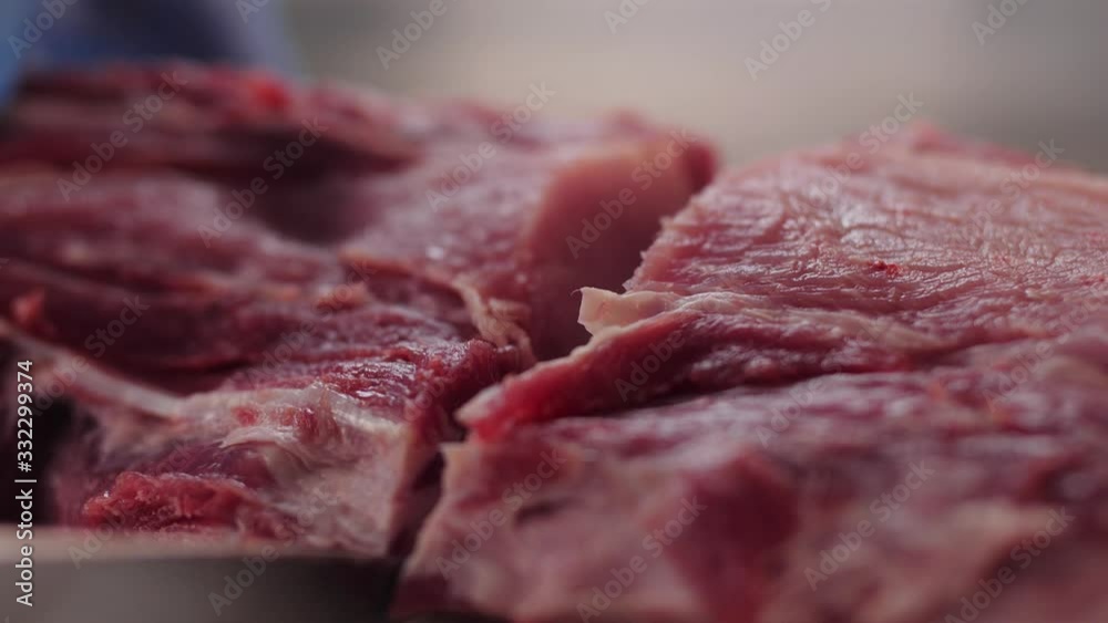 butcher in blue gloves cuts pork meat with knife on table