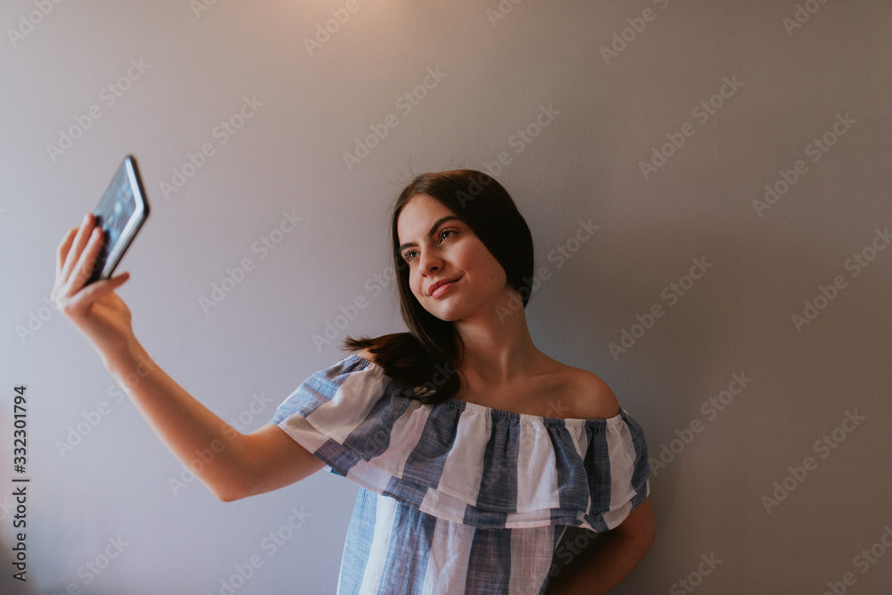 Naklejka premium A teenage girl with a phone takes selfies in her room