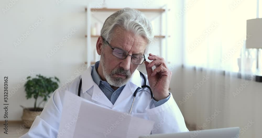 Concentrated serious old male doctor wearing white coat, stethoscope holding medical papers. Professional senior mature healthcare expert reading documents thinking of prescription, analyzing report. Concentrated serious old male doctor wearing white coat, stethoscope holding medical papers. Professional senior mature healthcare expert reading documents thinking of prescription, analyzing report.