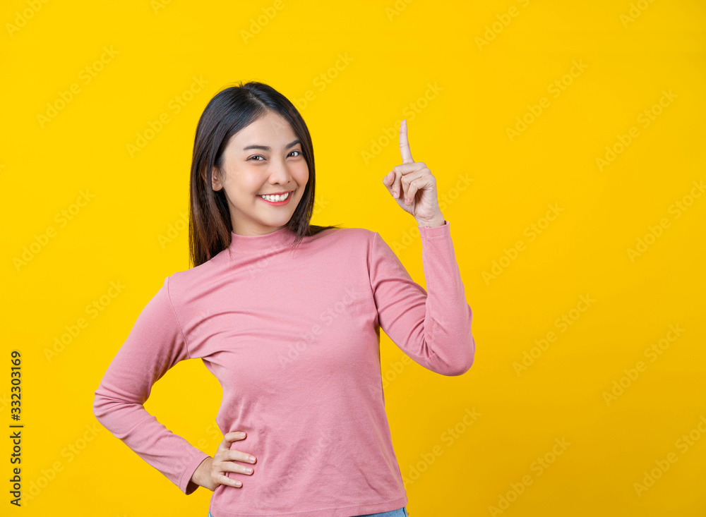 Asian smiling young woman finger Pointing up for advertise, banner or showing on isolated yellow color background, wearing winter cozy sweater indoors studio, happiness and fun, copy space concept Asian smiling young woman finger Pointing up for advertise, banner or showing on isolated yellow color background, wearing winter cozy sweater indoors studio, happiness and fun, copy space concept