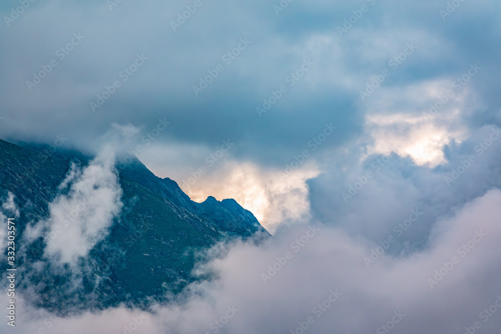 High mountain with rocky slopes hidden in clouds and fog.