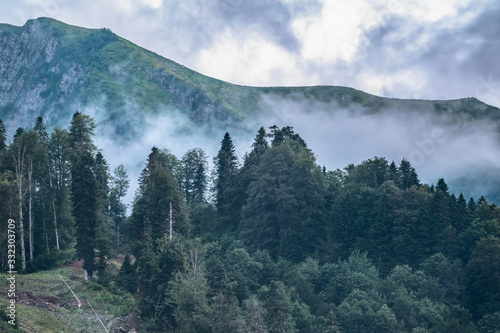 High mountain with green slopes hidden in clouds and fog.