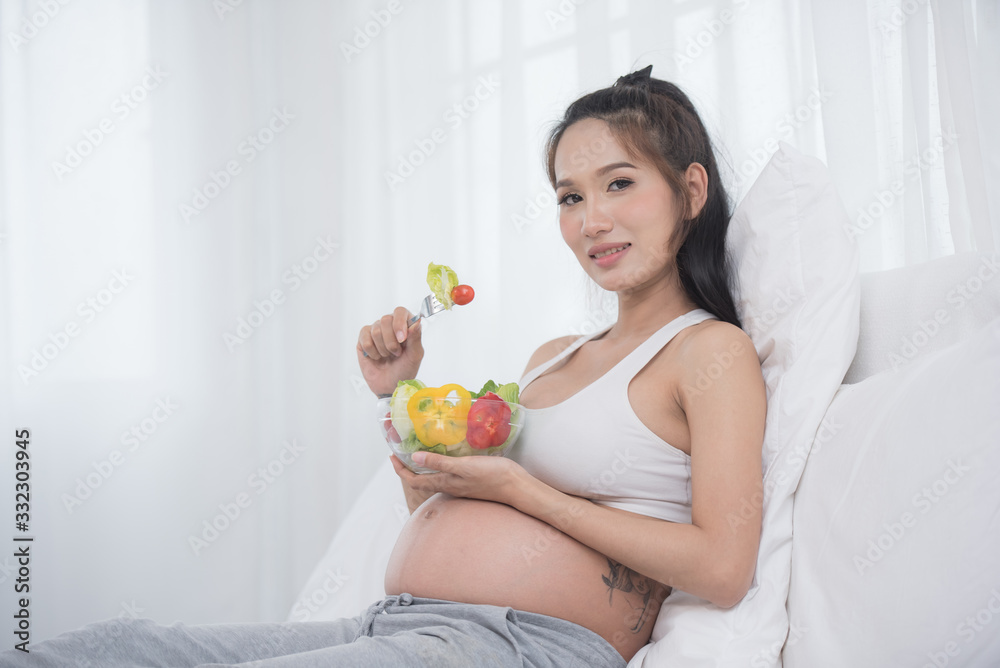 care about unborn child. pregnancy, healthy food and people concept, happy pregnant woman eating vegetable salad for breakfast sitting on bed at home. pregnancy and healthy organic nutrition. care about unborn child. pregnancy, healthy food and people concept, happy pregnant woman eating vegetable salad for breakfast sitting on bed at home. pregnancy and healthy organic nutrition.