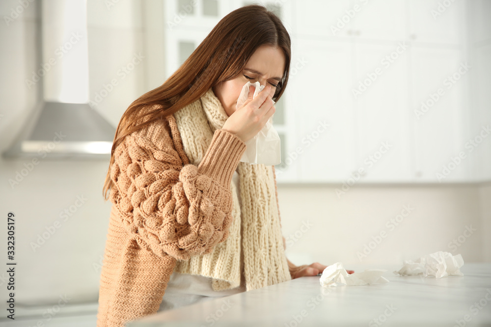 Sick young woman sneezing in kitchen. Influenza virus Sick young woman sneezing in kitchen. Influenza virus