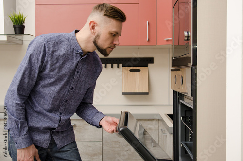 attractive bearded man peeks into an oven in a modern kitchen