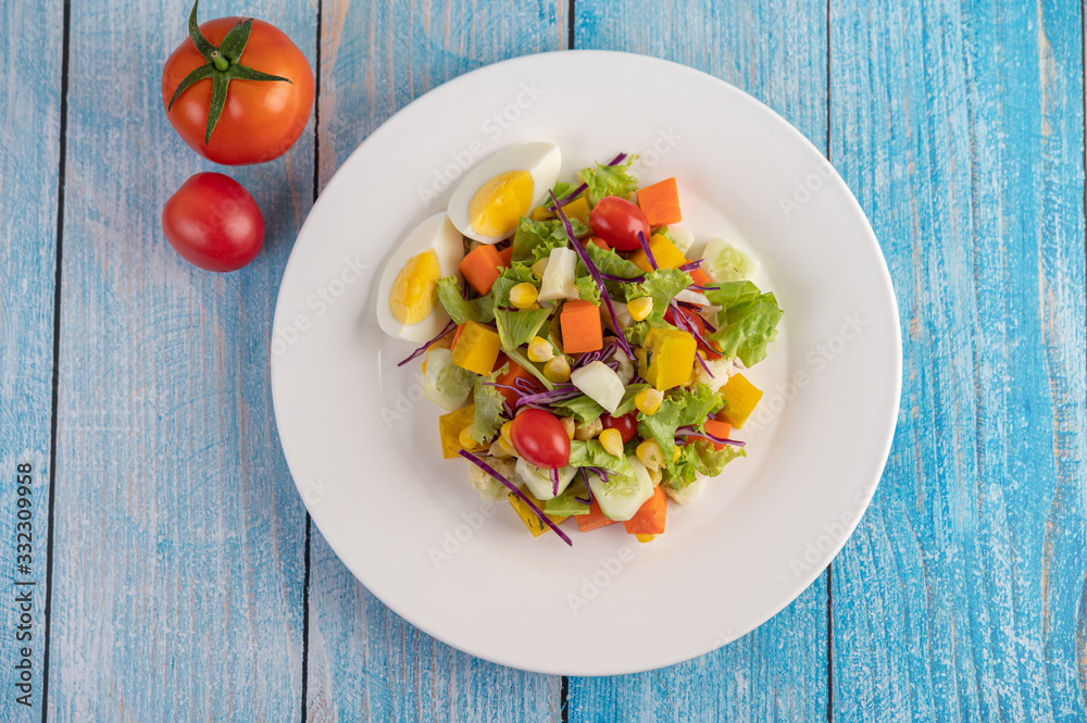 The salad is on a white plate, with a sandwich and tomatoes on the blue wooden floor. The salad is on a white plate, with a sandwich and tomatoes on the blue wooden floor.
