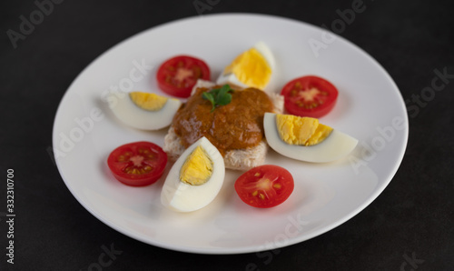 Bread topped with chili paste with boiled eggs and tomatoes on a white plate.