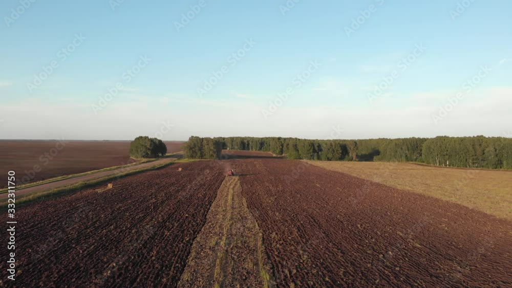 Drone camera approaching a red tractor riding in a field and plowing fertile soil in the countryside Drone camera approaching a red tractor riding in a field and plowing fertile soil in the countryside