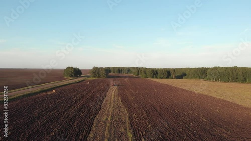 Drone camera approaching a red tractor riding in a field and plowing fertile soil in the countryside