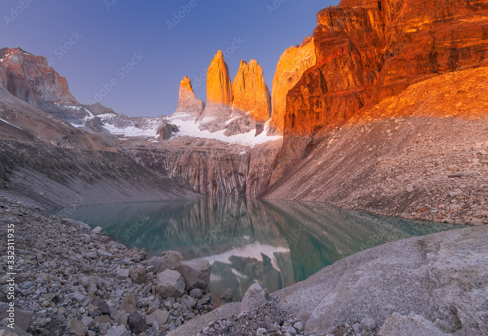 A beautiful red light sunset of the three Torres del Paine in front of a cold green lake from Mirador Base Torres del Paine.