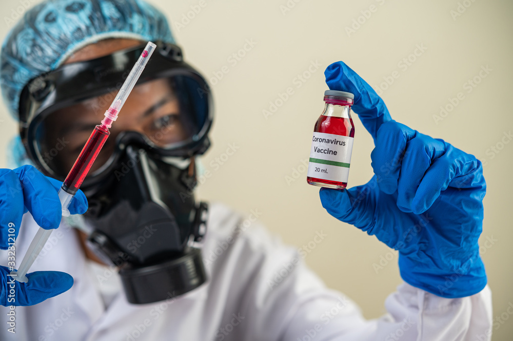 Scientists wearing masks and gloves Holding a syringe with a vaccine to prevent covid-19 Scientists wearing masks and gloves Holding a syringe with a vaccine to prevent covid-19